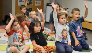 Young children in class raising their hands.